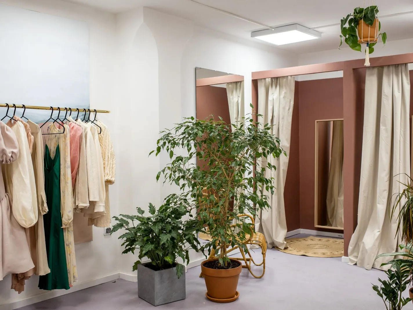 Loja com araras de roupas, cortinas claras e plantas